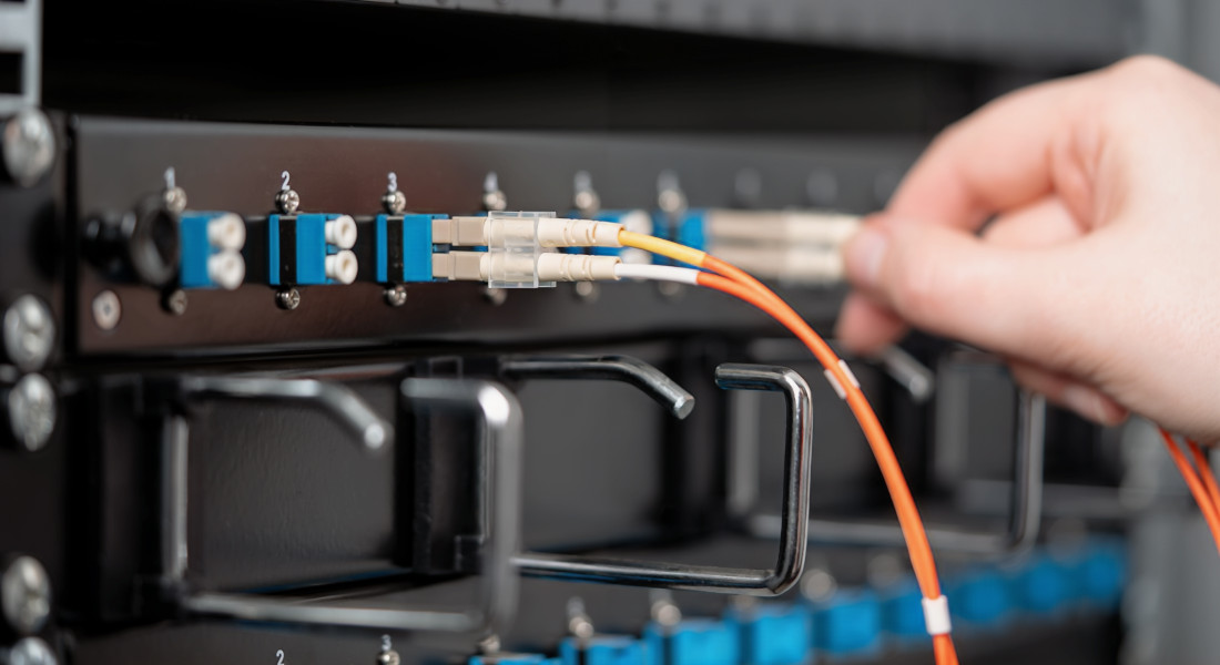 Close-up of a hand inserting a fiber optic cable into a patch panel with numbered connectors.
