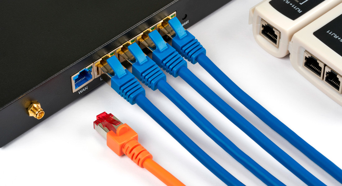 Netzwerk-Switch mit angeschlossenen blauen Netzwerkkabeln und einem orangefarbenen Netzwerkkabel.