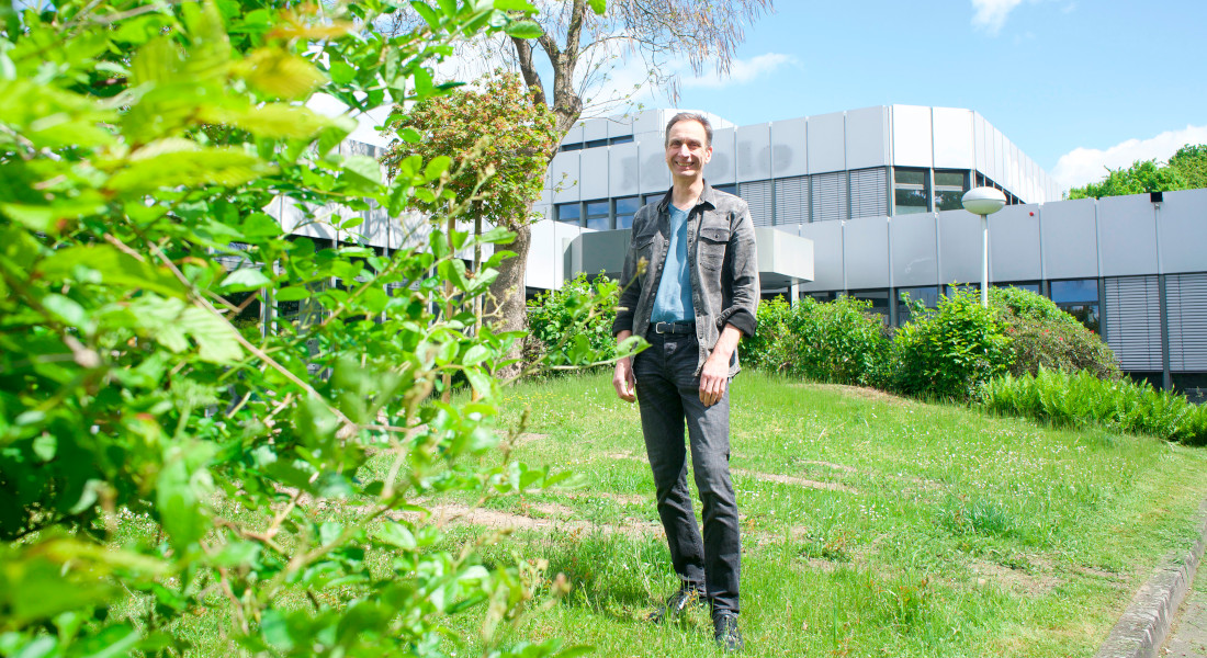 Mann steht in grüner Außenanlage vor einem modernen Gebäude