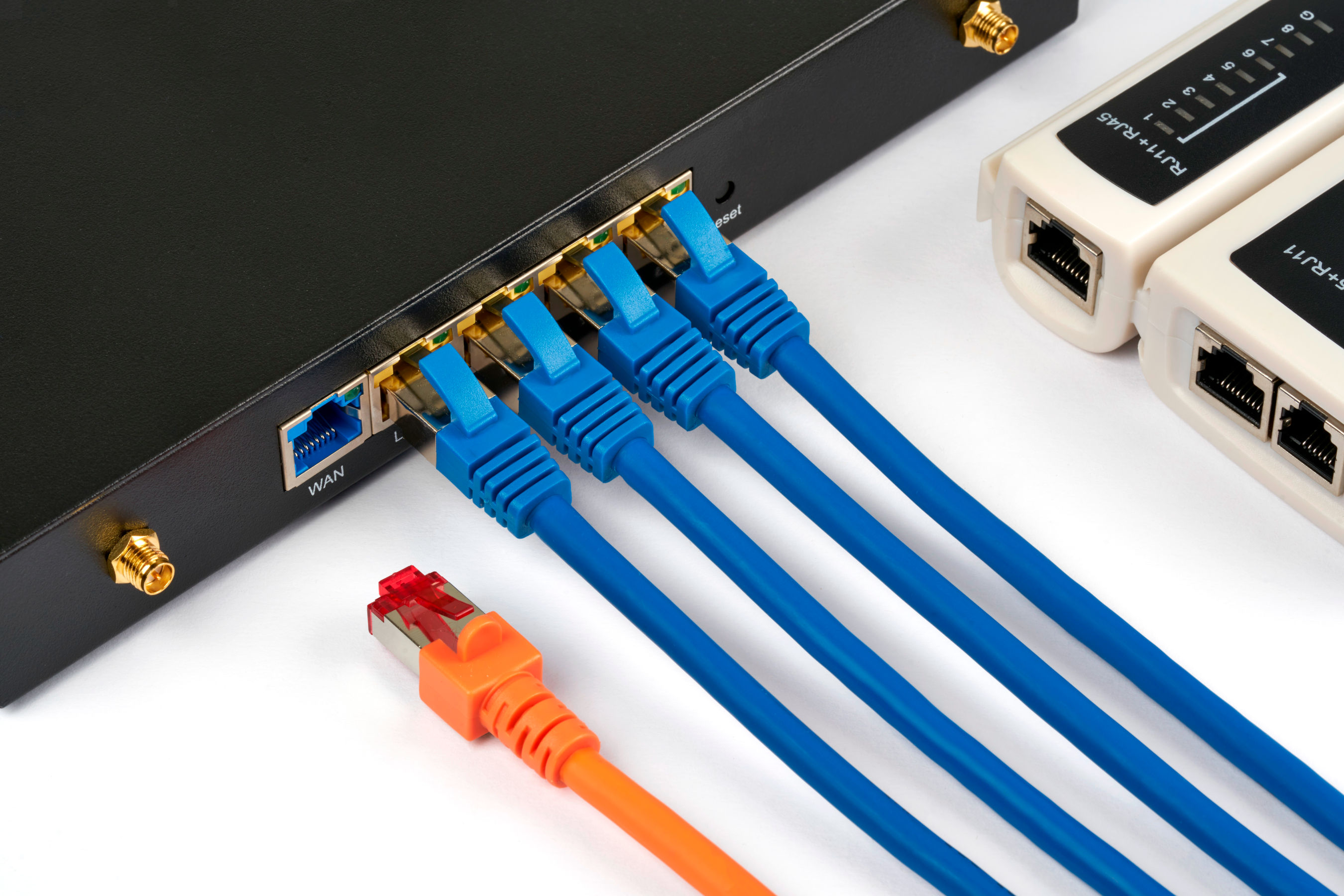 Netzwerk-Switch mit angeschlossenen blauen Netzwerkkabeln und einem orangefarbenen Netzwerkkabel.