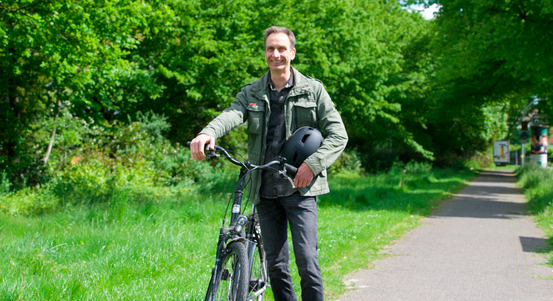 Mann mit Fahrrad und Helm steht auf einem Weg in grüner, bewaldeter Umgebung