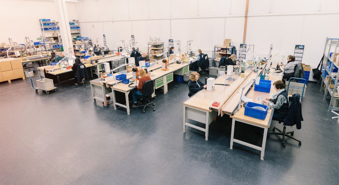 Produktionshalle mit mehreren Arbeitsplätzen, an denen Mitarbeiter Kabel bearbeiten.