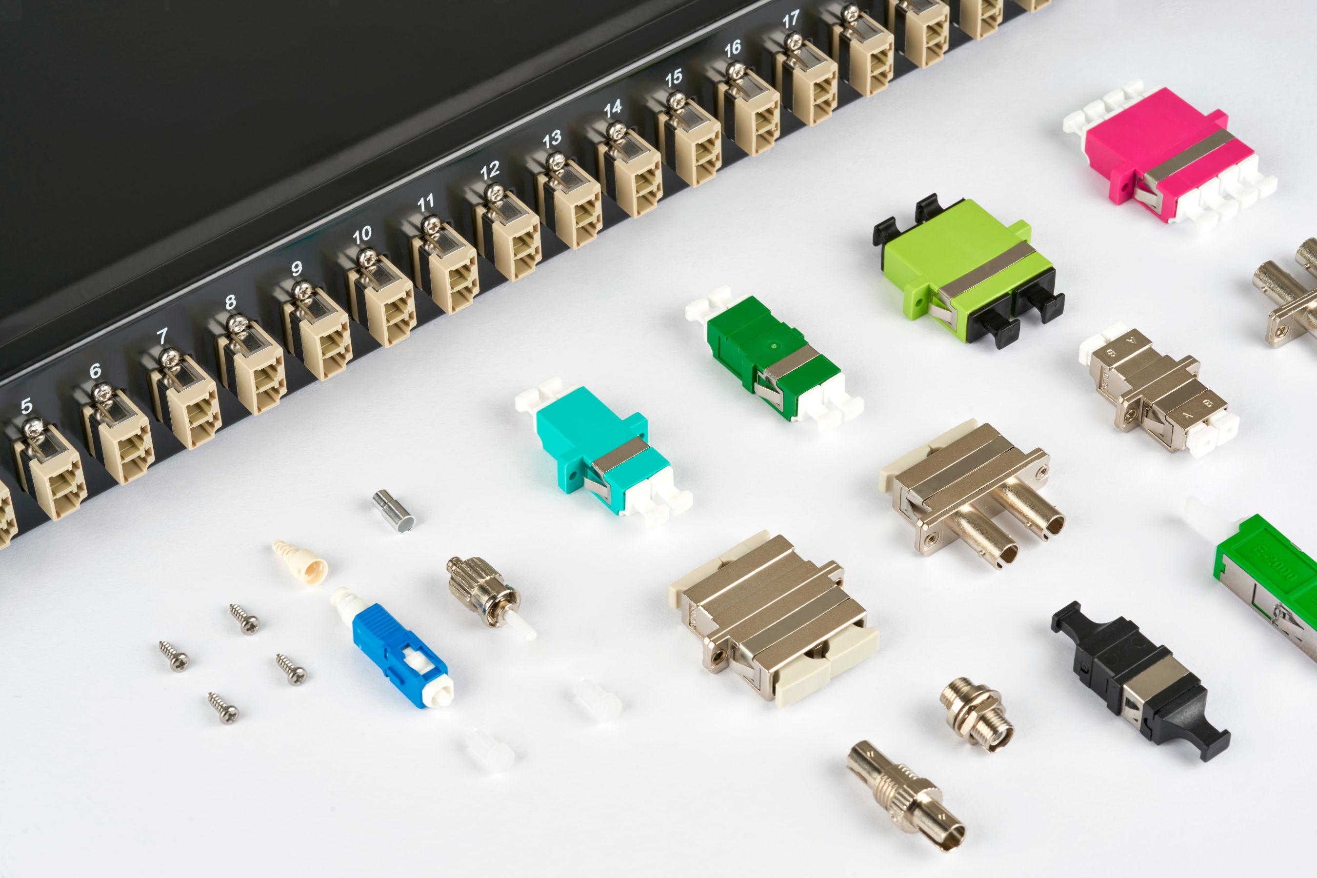 Various fiber optic connectors and couplers in front of a patch panel with numbered ports.