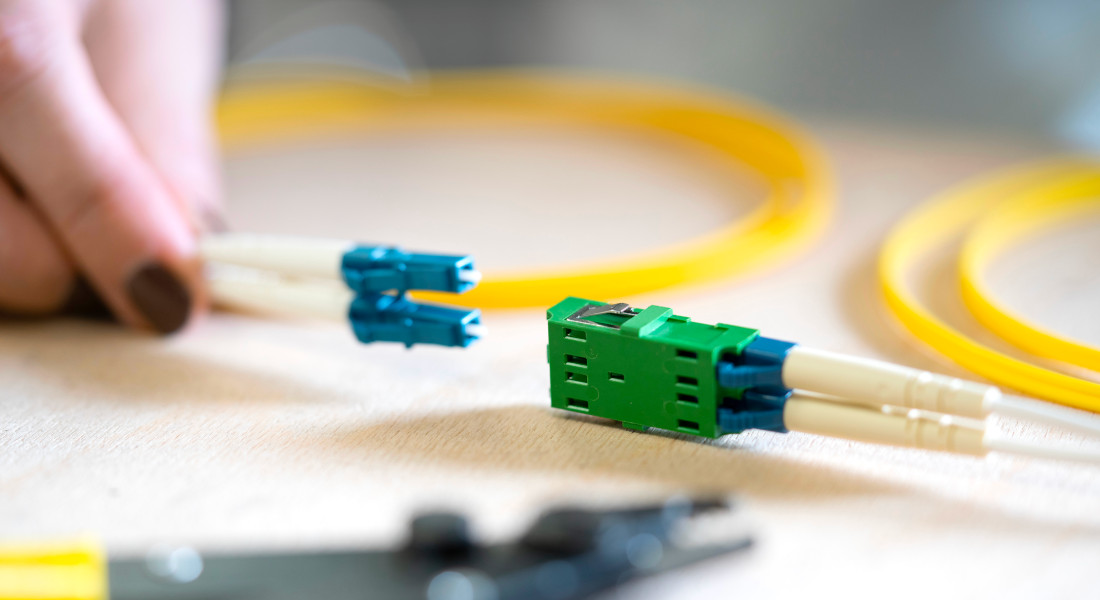 Hand holding fiber optic cable and green fiber optic coupling, yellow fiber optic cable in the background.