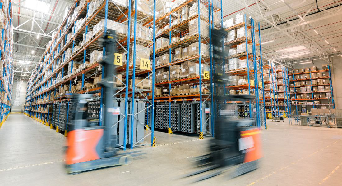 Warehouse with high shelves and cartons, fast-moving forklift truck in the foreground.
